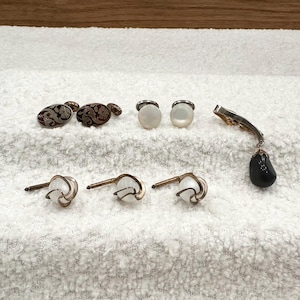 May include: An assortment of vintage cufflinks and a brooch. The cufflinks include two pairs with floral designs in red and black, and two pairs with white, round, mother-of-pearl faces. A silver-toned brooch with a black teardrop-shaped stone is also present.