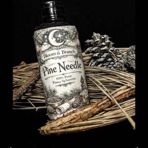 May include: A dark, vintage-style bottle of "Pine Needle" essential oil, with a black cap and a detailed label featuring botanical illustrations and the text "Bloom & Branch." The bottle rests on pine needles and is accompanied by pine cones.