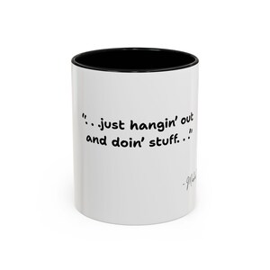 May include: A white ceramic mug with a black interior and rim. The exterior features the black text "..just hangin' out and doin' stuff.." followed by a signature that appears to read "~Michael" in a cursive script font.