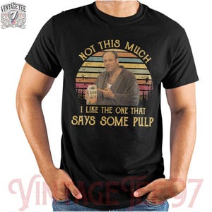 May include: Black t-shirt with a retro design featuring a man holding a juice box, with the text "NOT THIS MUCH I LIKE THE ONE THAT SAYS SOME PULP." The shirt also has a vintage logo on the upper left.