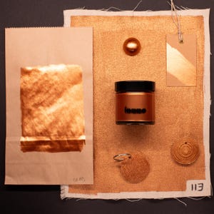 May include: A gold metallic paint in a jar with a black lid. The jar is labeled "loumo". The paint is surrounded by swatches of gold metallic paint on fabric, paper, and a small round piece of leather.