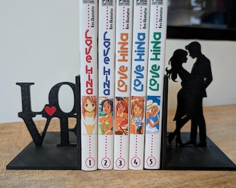 May include: Five volumes of the Love Hina manga series by Ken Akamatsu, published by Pika Edition, are held between two black metal bookends. The left bookend features the word LOVE with a red heart, and the right features a couple silhouette.