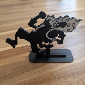 May include: A black 3D printed figurine of a dynamic character in a running pose, featuring a white cloud-like accent trailing from the head and shoulders. The figure is mounted on a flat, rectangular black base for stability and display.