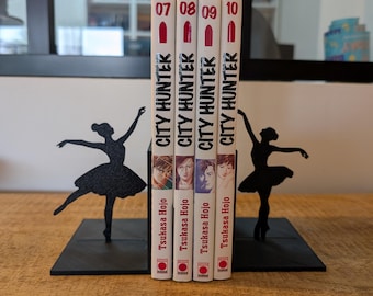 May include: Four volumes of the City Hunter manga series, numbered 07 through 10 by Tsukasa Hojo, are held between two black metal bookends. Each bookend features a silhouette of a ballerina in a dancing pose with a textured, glittery finish.