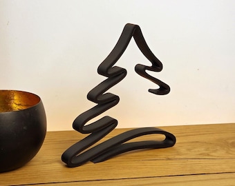 May include: A black metal Christmas tree sculpture with a unique, stylized design. The tree is made of a continuous, curved line, creating a modern and minimalist aesthetic. The sculpture is displayed on a wooden surface.