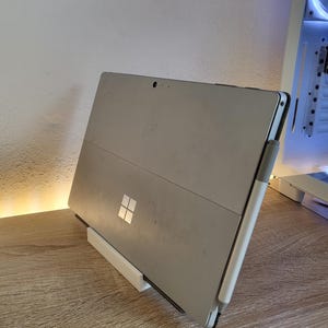 May include: A silver laptop computer with a white stand and a white stylus. The laptop is on a wooden surface.