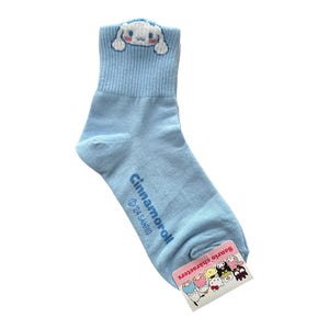May include: Light blue ankle socks with a white Cinnamoroll character on the top and a tag with other Sanrio characters on the bottom. The socks say "Cinnamoroll" and "Sanrio Characters".