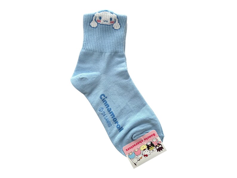 May include: Light blue ankle socks with a white Cinnamoroll character on the top and a tag with other Sanrio characters on the bottom. The socks say "Cinnamoroll" and "Sanrio Characters".