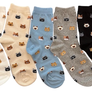 Puede incluir: Cinco pares de calcetines en varios colores: blanco roto, beige, azul claro, gris y negro. Cada calcet&iacute;n presenta un patr&oacute;n repetido de caras de gato en diferentes colores. Los gatos tienen pelaje negro, marr&oacute;n y canela.