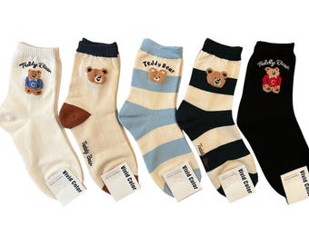 May include: Five pairs of socks with a teddy bear design. The socks are striped in blue and white, black and white, and brown and white. The socks have the text "Teddy Bear" and "Vivid Color" on the tags.