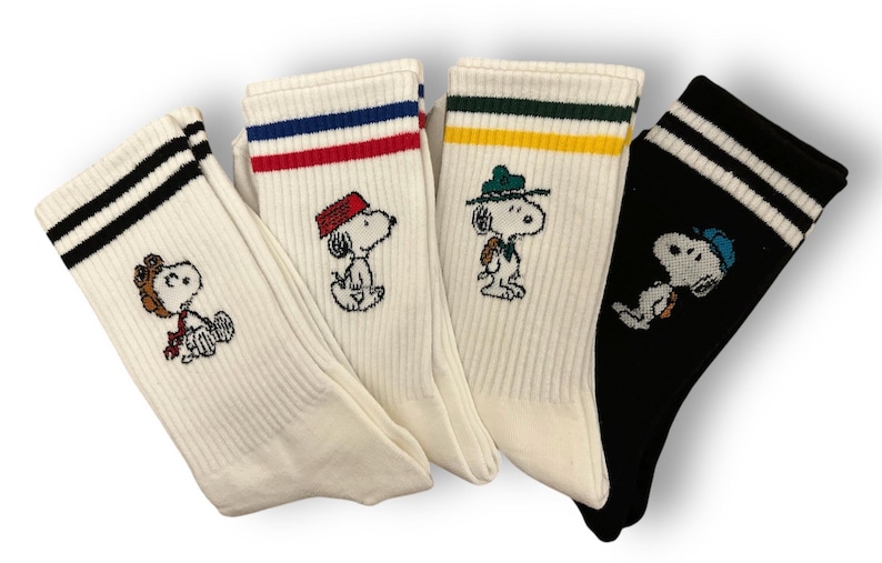 May include: Four pairs of white and black striped crew socks with different embroidered Peanuts characters. The characters are wearing different hats and outfits.