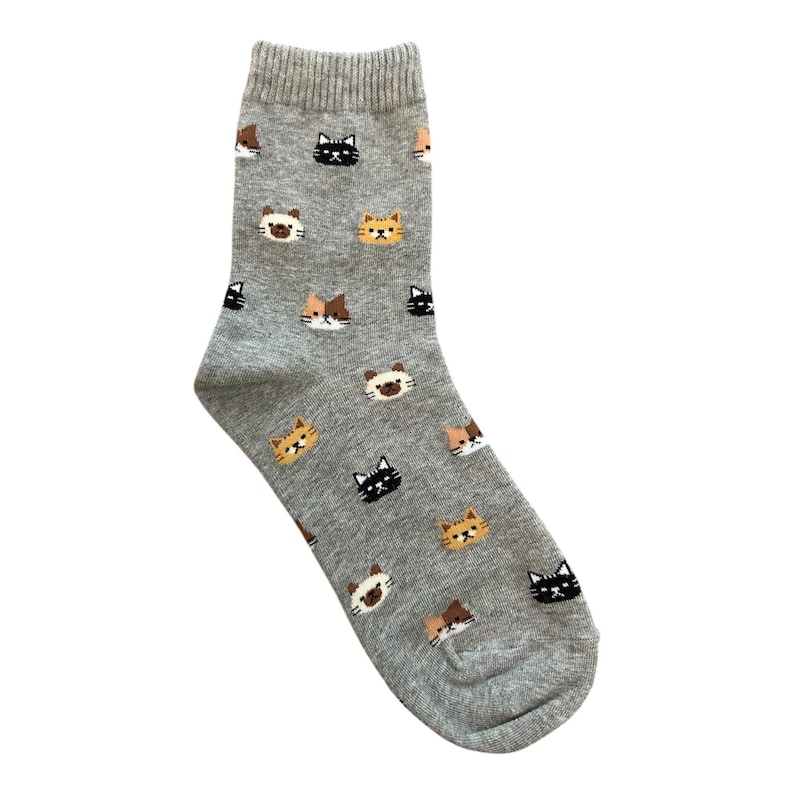 Puede incluir: Un calcet&iacute;n gris con un patr&oacute;n repetido de caras de gato en negro, marr&oacute;n y amarillo. El calcet&iacute;n tiene un pu&ntilde;o acanalado y est&aacute; hecho de un material suave. Las caras de los gatos est&aacute;n espaciadas uniformemente.