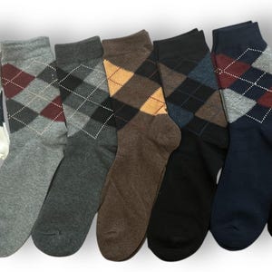 May include: A set of seven crew-length socks arranged in a row, each featuring a classic argyle diamond pattern. The colours include white, light grey, dark grey, brown, black, navy blue, and black, all with contrasting diamond outlines.