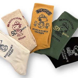 May include: Four pairs of white, yellow, green, and black socks with a cartoon dog wearing a scout hat and the text "BEAGLE SCOUTS" and "50 years" on them.