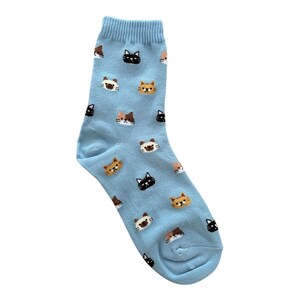 Puede incluir: Un calcet&iacute;n azul claro con un patr&oacute;n repetido de caras de gato en negro, marr&oacute;n y naranja. El calcet&iacute;n est&aacute; hecho de un material suave y est&aacute; dise&ntilde;ado para adaptarse al pie. Un accesorio divertido y juguet&oacute;n.