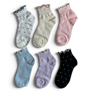 May include: A set of six ankle socks featuring ruffled cuffs and polka dot patterns. The colours include white with black dots, cream with pink dots, solid pink, light blue with white dots, light purple with white dots, and black with white dots.