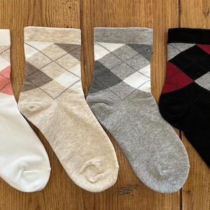Op de afbeelding: Vier paar sokken met ruitpatroon in verschillende kleuren. De sokken zijn wit met roze en bruine ruiten, bruin met bruine ruiten, grijs met witte ruiten en zwart met rode en grijze ruiten.