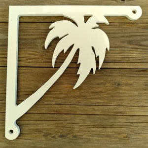 May include: White wooden shelf bracket with a palm tree cutout design. The bracket is mounted on a wooden surface.
