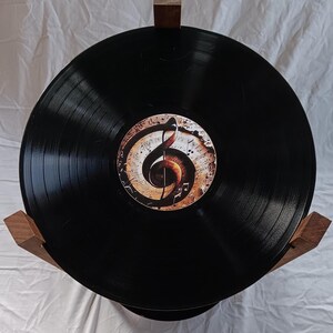 May include: A black vinyl record with a brown and gold treble clef design on the label. The record is mounted on a wooden stand.