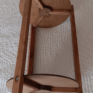 May include: A wooden side table with a round top and three legs. The table is made of light brown wood and has a simple design.