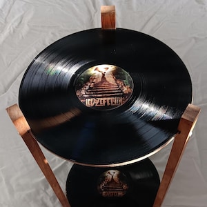 May include: A two-tiered wooden stand holding two black vinyl records. The top record features a central label with an illustration of a staircase leading towards a bright light and the text Led Zeppelin. The bottom record has an identical label.