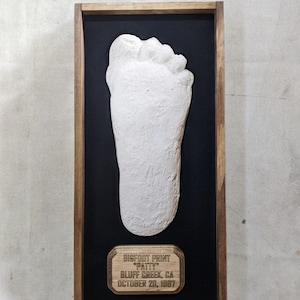 May include: A framed plaster cast of a Bigfoot footprint, with a wooden plaque that reads "Bigfoot Print "Patty" Bluff Creek, CA October 20, 1987".