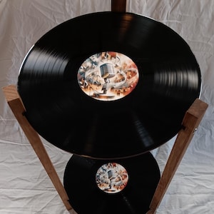 May include: A two-tiered wooden stand with two black vinyl records. The top record has a colorful label with a microphone and musical notes. The bottom record has a similar label with a microphone.
