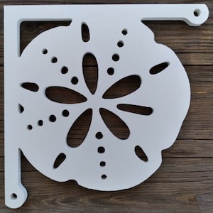 Puede incluir: Soporte de estante de madera blanco con un diseño recortado de un dólar de arena. El soporte está montado en una superficie de madera.