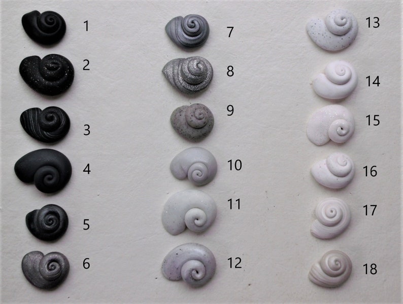 Peut inclure: Dix-huit coquillages en c&eacute;ramique de diff&eacute;rentes nuances de gris, noir et blanc, dispos&eacute;s en trois rang&eacute;es de six. Les coquillages sont num&eacute;rot&eacute;s de 1 &agrave; 18.