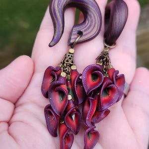 May include: A pair of purple and gold wood ear gauges with dangling red and purple flower charms.