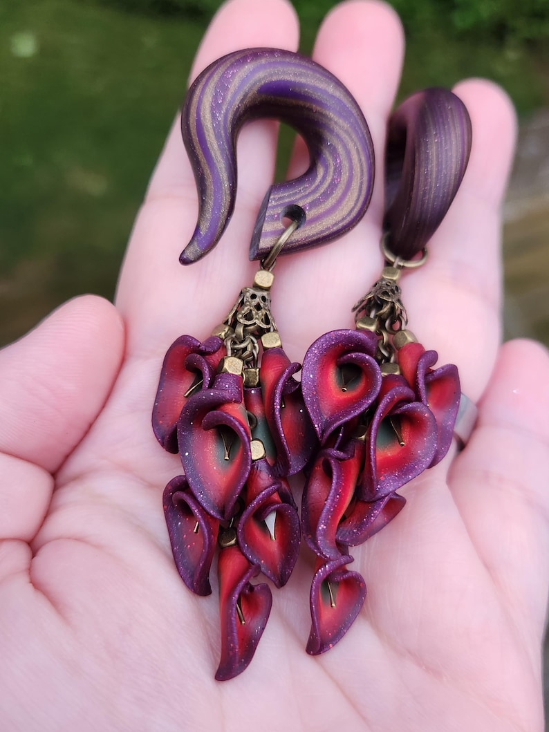 May include: A pair of purple and gold wood ear gauges with dangling red and purple flower charms.