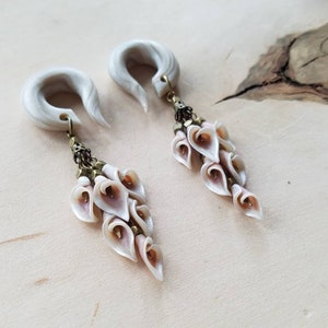 May include: A pair of white faux bone ear gauges with a dangling charm of white and pink flower-shaped beads.