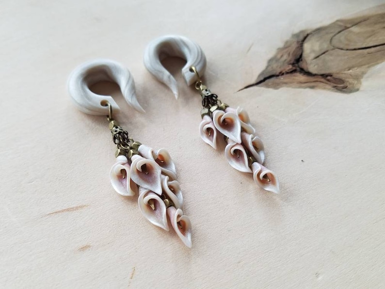 May include: A pair of white faux bone ear gauges with a dangling charm of white and pink flower-shaped beads.