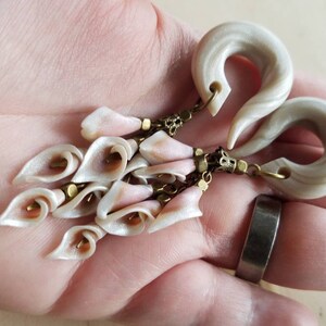 May include: A pair of white and gray swirl ear gauges with a dangling chain of white and pink flower-shaped charms.
