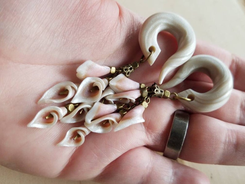 May include: A pair of white and gray swirl ear gauges with a dangling chain of white and pink flower-shaped charms.