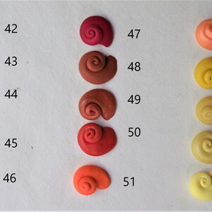 Peut inclure: Un ensemble de 14 petites coquilles d'escargots en c&eacute;ramique artisanales dans diff&eacute;rentes nuances de rouge, orange et jaune. Les coquilles sont num&eacute;rot&eacute;es de 42 &agrave; 56.