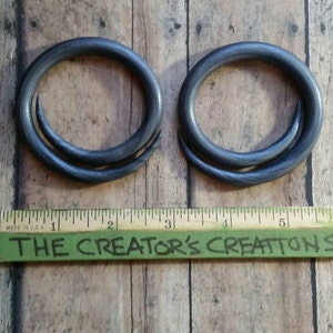 Peut inclure: Deux boucles d'oreilles en m&eacute;tal noir avec un design torsad&eacute;. Les boucles d'oreilles sont pr&eacute;sent&eacute;es sur une surface en bois avec une r&egrave;gle qui indique "The Creator's Creations".