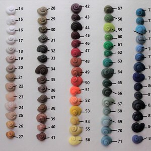 May include: A color chart of 100 small, ceramic snail-shaped beads. The beads are arranged in rows of 10, with each row featuring a different color. The colors range from black to white, with shades of gray, brown, red, orange, yellow, green, blue, purple, and pink.