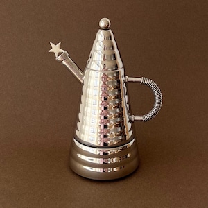 May include: A white ceramic mug with a black handle and the text "But First, Coffee" in a bold, black font. The mug is set against a blurred background, suggesting a cozy setting.