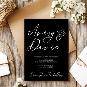 May include: Black wedding invitation with white script text. The invitation reads "Avery & Davis" and includes the wedding date, time, and location. The invitation is on a wooden surface with flowers and an envelope.