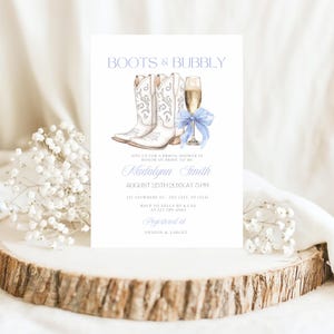 May include: A white bridal shower invitation with a watercolor illustration of two white cowboy boots and a glass of champagne with a blue ribbon. The text on the invitation reads "Boots & Bubbly", "Join us for a bridal shower in honor of bride to be Madalynn Smith", "August 25th 20XX at 5 PM", "123 Anywhere St. Any City, ST 12345", "RSVP to Belly by A.Lan at 123 789-4560", and "Registered at Amazon & Target".
