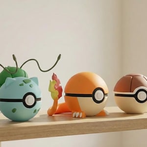Puede incluir: Tres figuras de personajes coloridos, que se asemejan a Pokémon, se exhiben en una estantería de madera. Las figuras incluyen un Bulbasaur azul claro, un Charmander naranja con una llama y un Squirtle marrón. Cada figura es redonda con un detalle de círculo blanco y negro.
