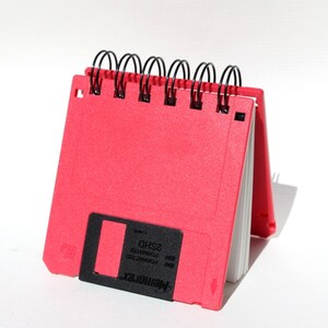 May include: A red notebook shaped like a floppy disk with a black label that reads "MEMORYMAX 3.5" and "FORMATTED IBM PC-DOS 2SHD".