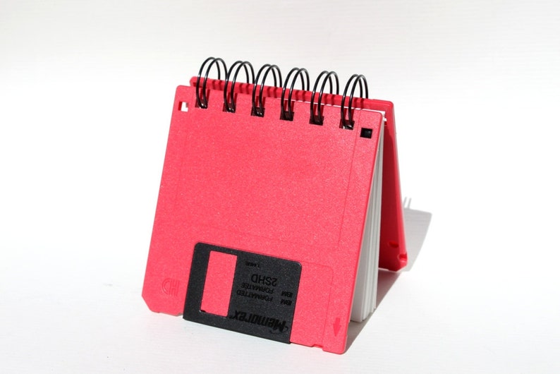 May include: A red notebook shaped like a floppy disk with a black label that reads "MEMORYMAX 3.5" and "FORMATTED IBM PC-DOS 2SHD".
