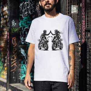 May include: White t-shirt with a graphic of two people riding motorcycles and high-fiving each other.