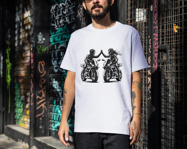 May include: White t-shirt with a graphic of two people riding motorcycles and high-fiving each other.