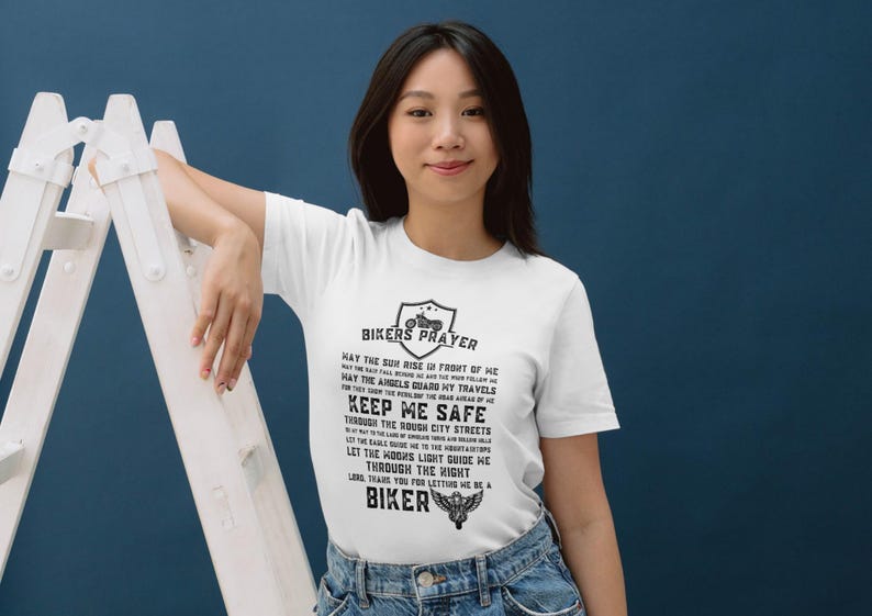 May include: White t-shirt with a black print of a biker prayer. The text reads "Bikers Prayer" and includes a motorcycle graphic. The text continues with "May the sun rise in front of me, May the rain fall behind me, May the angels guard my travels, Keep me safe through the rough city streets, Let the hogs light guide me, Let the roads lead me the right way, Thank you for letting me be a biker."