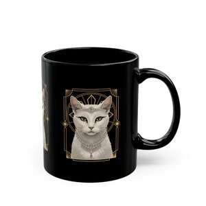 May include: Black ceramic mug featuring a white cat illustration wearing a jeweled headband and necklace. The cat is framed within a gold art deco design. The mug has a curved handle.