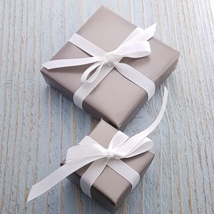 Op de afbeelding: Twee grijze cadeaudozen met witte satijnen strikken. De dozen zijn in elkaar genest.