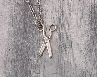 Op de afbeelding: Een zilveren ketting met een klein, gedetailleerd schaar-hanger.